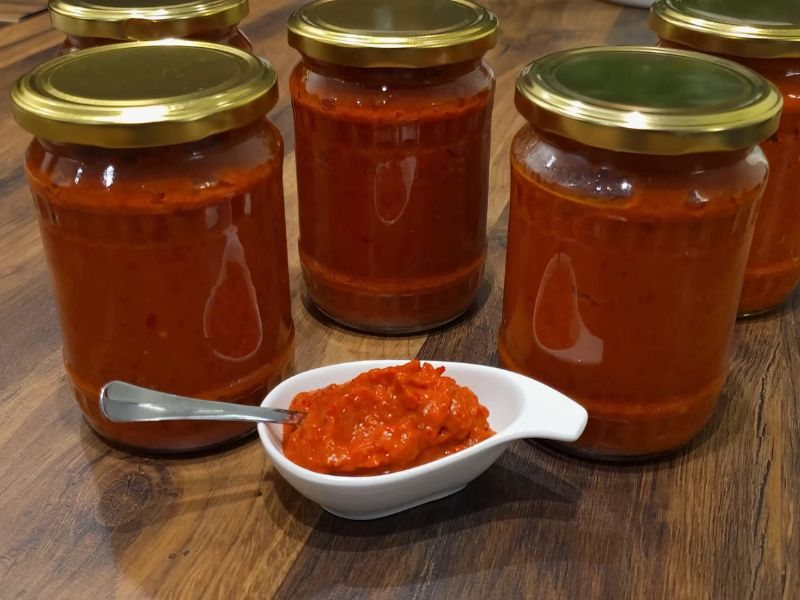 četri teglice ajvara sa činijom sa ajvarom pored